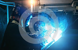 Industrial steel welder in process of work in metal factory. Sparks and smoke fly from welding