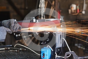 Industrial tool worker grinds a square steel pipe on a rotating belt sander