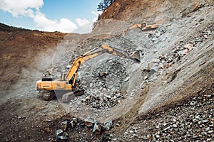 Industrial track type excavator digging and loading ore in a dumper truck at a quarry