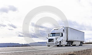 Industrial transportation big rig white semi truck transporting frozen cargo in reefer semi trailer running on the road with