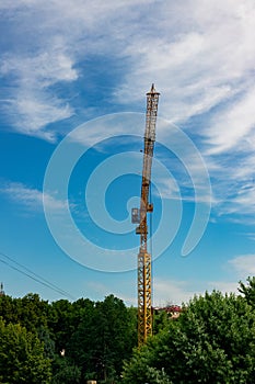 industrial versus nature concept vertical photography of construction crane above green foliage in summer clear weather