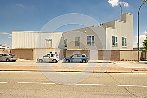 Industrial warehouse facade with white roof, cement wall, windows and parked private cars on a sunny day