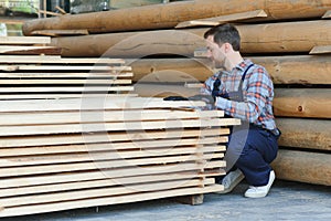 Industrial warehouse of a sawmill, an employee puts his hands on the finished products at the sawmill in the open air.