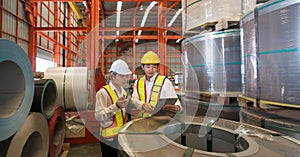 Industrial warehouse scene featuring two safety-conscious men inspecting steel sheet roll stack, imbued with the raw essence of