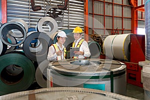 Industrial warehouse scene featuring two safety-conscious men inspecting steel sheet roll stack, imbued with the raw essence of