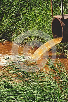 Industrial waste in form orange water flowing from pipe into river