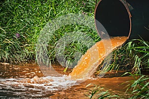 Industrial waste in form orange water flowing from pipe into river