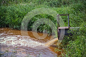 Industrial waste in form orange water flowing from pipe into river