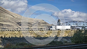 Industrial white big rig long haul semi truck with dry van semi trailer running on the road with lifting bridge and autumn hills