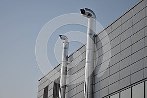 Industrial white building with sheet metal facade of repeating rectangle paneling. on wall are two silver-shiny chimney pipes with