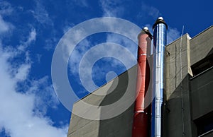 Industrial white building with sheet metal facade of repeating rectangle paneling. on wall are two silver-shiny chimney pipes with