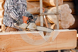 Industrial work carpenter sawing with chainsaw log, construction frame building site of house made of wood