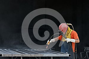 Industrial worker cleaning surface of steel with sandblast