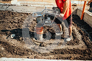 industrial worker compacting soil in house foundation using compactor
