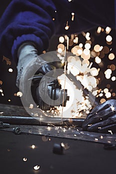 Industrial worker cutting metal pipe with many sparks baubles in the background