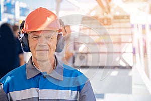 Industrial worker engineer man in protective helmet and headphones in uniform on background of factory sunlight