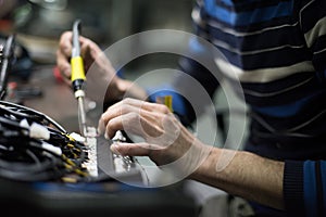 Industrial worker man soldering cables of manufacturing equipment in a factory. Selective focus