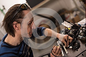 Industrial worker man soldering cables of manufacturing equipment in a factory. Selective focus