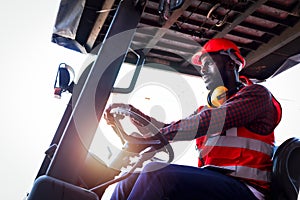Industrial worker man wearing safety bright neon red vest and helmet driving forklift car at plant factory industry, African