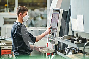 Industrial worker operating cnc machine in protective mask at metal machining industry