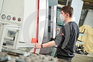 Industrial worker operating cnc machine in protective mask at metal machining industry