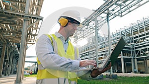 Industrial worker is operating a laptop outside of the oil refinery