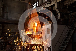 Industrial worker oversees molten metal pouring in foundry. Steelworker in protective gear at metal manufacture. Heavy