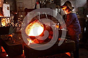 Industrial worker pours molten metal at foundry. Steel production in heat-resistant suit, helmet. Heavy industry labor