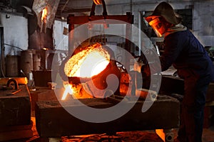 Industrial worker in protective gear pours molten metal at steel foundry. Manufacturing process in heavy industry with