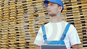 Industrial worker in uniform checking large wooden box on tablet in warehouse