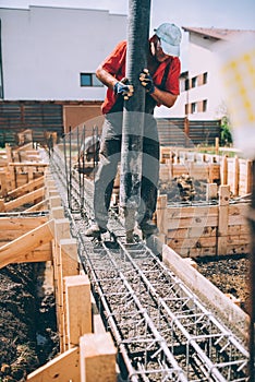 Industrial worker using concrete pump for pouring concrete into foundation