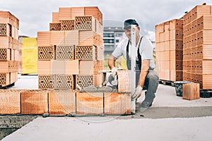 Industrial worker using trowel and hammer for building exterior walls with bricks and mortar