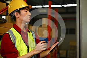 Industrial worker wearing hard hat checking stock and order details in warehouse. Distribution center and logistic