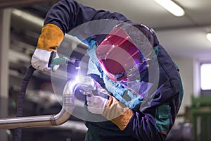 Industrial worker welding in metal factory.