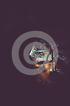 Industrial worker welding round pipe on a work table, producing smoke, sparks and colorful reflections