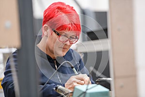 Industrial worker woman soldering cables of manufacturing equipment in a factory