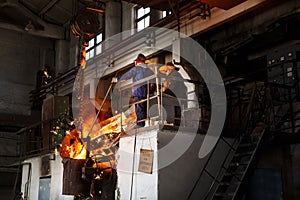 Industrial workers in protective gear operate furnace, handling molten metal at steel mill. Teamwork in heavy industry