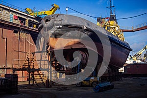 Industrial workers repair fishing boat in dry dock. Maintenance of marine vessel hull, welding, painting under blue sky