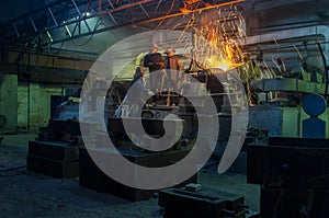 Industrial workers team pouring molten metal at foundry. Steel mill laborers handling manufacturing process in workshop