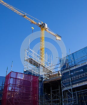 Industrial yellow crane and scaffolding on building site against blue sky