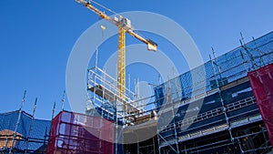 Industrial yellow crane and scaffolding on building site against blue sky wide image