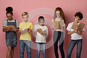 Industrious diverse children reading school textbooks on pink background