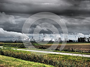 Industry, smoke stacks and wind turbines behind a green field under dark clouds near Antwerp