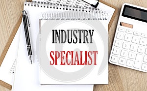 INDUTRY SPECIALIST is written in white notepad near a calculator, clipboard and pen. Business concept