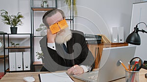 Inefficient tired lazy business man working sleeping on laptop computer with eyes stickers on face