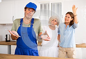 Inept plumber throws up his hands. In background, disgruntled apartment owners scold him photo