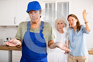 Inept plumber throws up his hands. In background, disgruntled apartment owners scold him photo