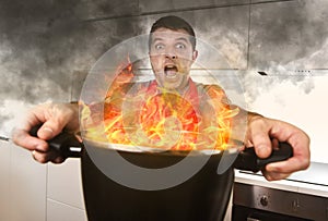 Inexperienced home cook with apron holding pot burning in flames with stress panic face expression