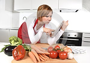 Inexperienced home cook woman in apron at kitchen using digital tablet as recipe reference