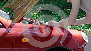 An inexperienced man approaches the open hood of broken car and and tries to repair it on his own